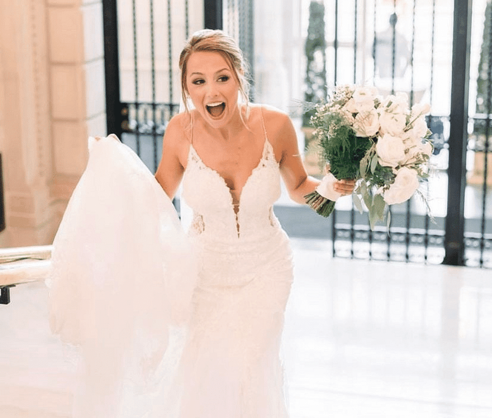 Excited bride holding a bouquet with her veil trailing behind.